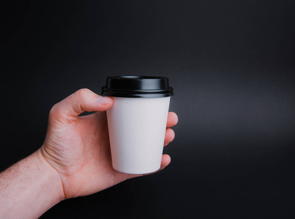Une main masculine tenant une tasse blanche avec couvercle en plastique noir sur fond sombre isolé
  - Photo, image