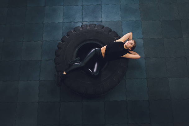 Powerful, attractive muscular girl engaged in gym, training with giant tires in the gym. Athlete resting after a hard workout. Exercise with heavy weight in the gym. - Foto, Bild
