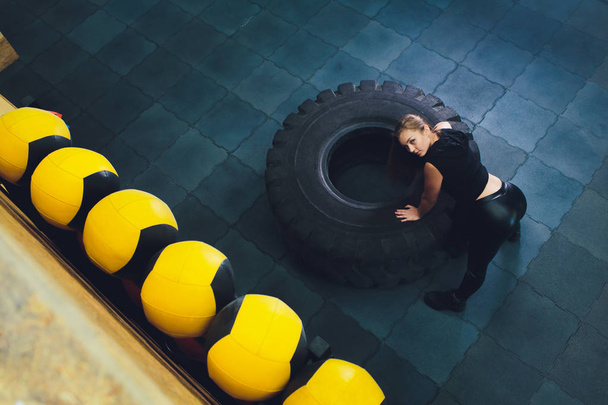 Fit female athlete working out with a huge tire, turning and carry in the gym. woman exercising with big tire. - Φωτογραφία, εικόνα