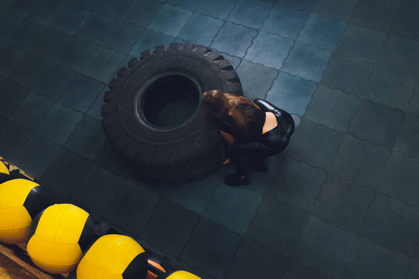 Fit female athlete working out with a huge tire, turning and carry in the gym. woman exercising with big tire. - Photo, Image