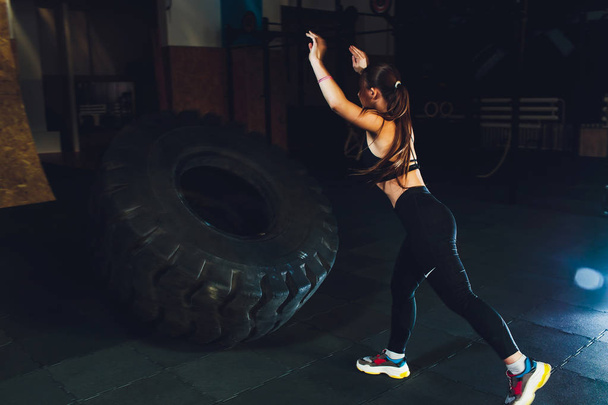 Fitness woman flipping wheel tire in gym. Fit female athlete working out with a huge tire. Back view. Sportswoman doing an strength exercise training. - Φωτογραφία, εικόνα