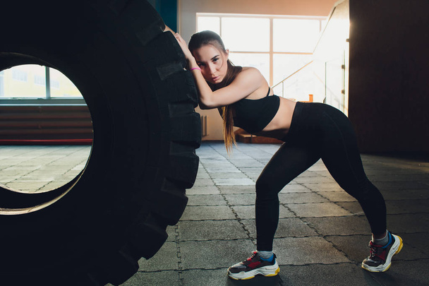 Fitness-Frau kippt Reifen in Turnhalle. fitte Athletin, die mit einem riesigen Reifen trainiert. Rückseite. Sportlerin beim Krafttraining. - Foto, Bild