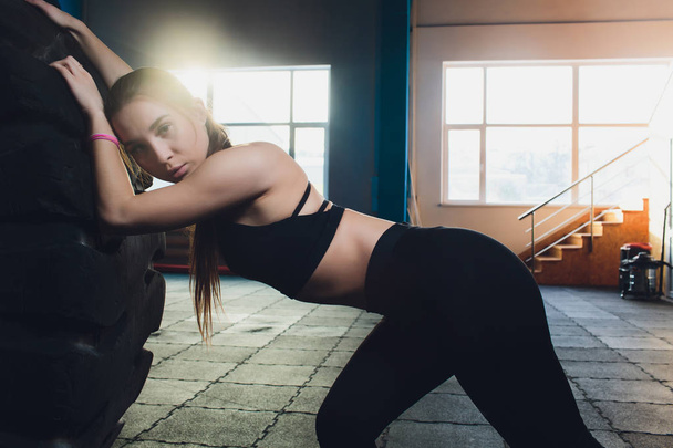 Fitness woman flipping wheel tire in gym. Fit female athlete working out with a huge tire. Back view. Sportswoman doing an strength exercise training. - Фото, зображення
