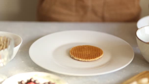 A woman prepares a delicious Breakfast in the morning in the kitchen, hands puts round fresh thin waffles on a white large plate, closeup - Imágenes, Vídeo
