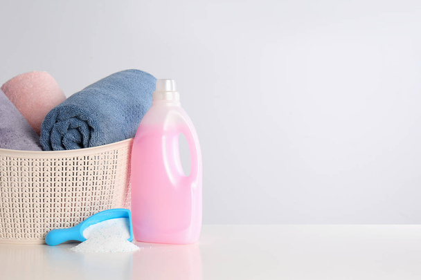Detergentes y cesta con toallas limpias sobre fondo blanco, espacio para texto. Día de lavandería
 - Foto, imagen