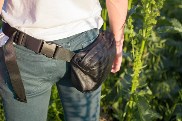 Young male traveler with belt bag stand in the fields against city - Fotoğraf, Görsel