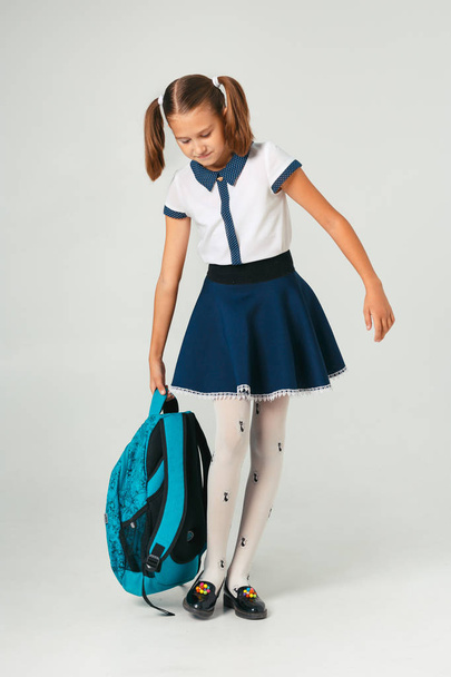 School meisje in uniform bedrijf een zware rugzak. Het probleem van de weging student accessoires - Foto, afbeelding
