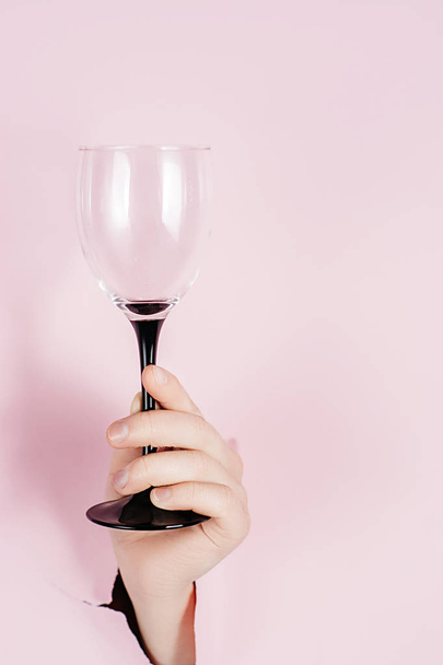Female hand holds wine glass is seen through a hole in torn pink paper. Overhead view, copy space. Holiday and birthday concept. - Фото, зображення