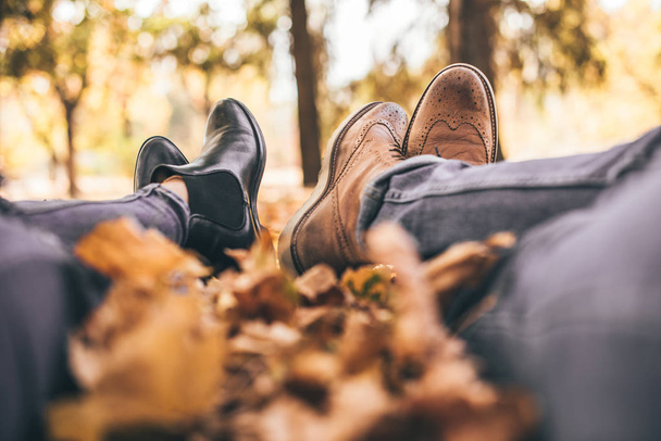 Um casal elegante está deitado no parque mostrando suas botas
 - Foto, Imagem