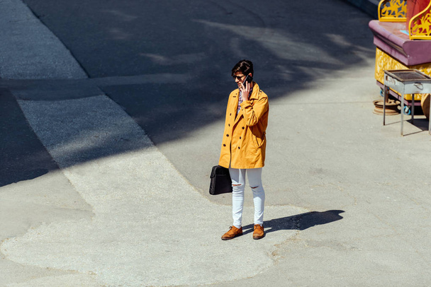 Şehir meydanında cep telefonuyla konuşan sarı ceketli bir işadamı. - Fotoğraf, Görsel