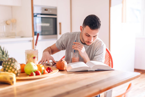 healthy strong young man reading a book early in the morning while making his smoothie. - Foto, Imagem