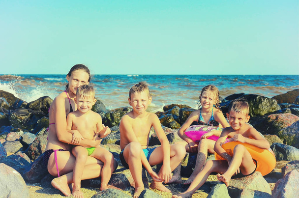 Anyu a gyerekekkel a tengeren a tengerparton a strandon, a víz veri a köveket. Tónusú Vintage fénykép. - Fotó, kép