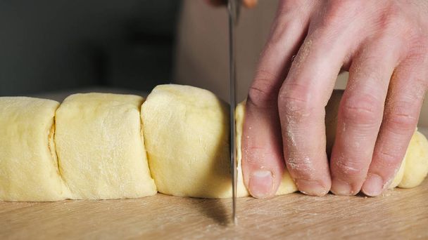 Baker chef corta rollo con canela, azúcar y mantequilla en porciones para hornear rollos de canela
. - Foto, Imagen