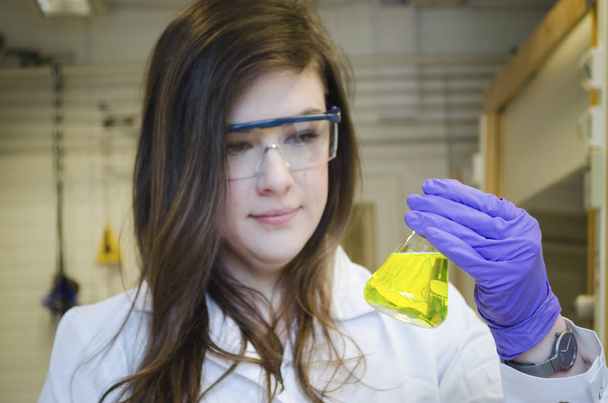 Kadın bilim adamı yetenekli sarı kolyeyi tutuyor ve dikkat ediyor. - Fotoğraf, Görsel
