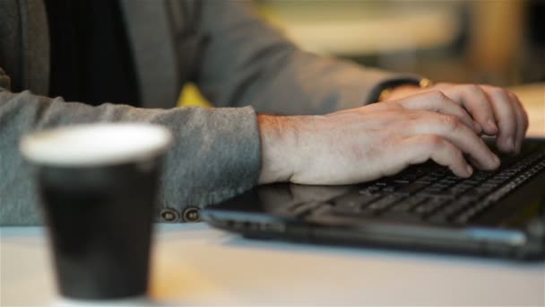 Κοντινό θέα του ελεύθερου δουλεύοντας στη χωροθέτηση φορητού υπολογιστή στο Internet Cafe σε εσωτερικούς χώρους. Νέος άνθρωπος με γένια είναι γράφοντας κείμενο πατώντας κουμπιά στο laptop. Online εργασία, ανεξάρτητος, γραφείο. - Πλάνα, βίντεο