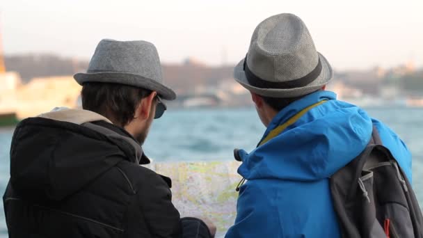 Dos turistas hombre examina mapa en la costa del mar
 - Imágenes, Vídeo