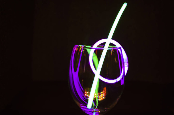 Blue and green glow stick on a wine glass and colourful light re - Foto, Bild