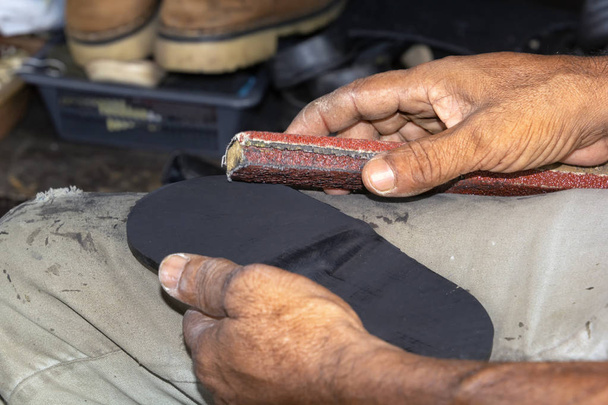 Shoemaker kiillottaa vanhojen lenkkareiden pohjaa työpajassa. lähikuva
 - Valokuva, kuva