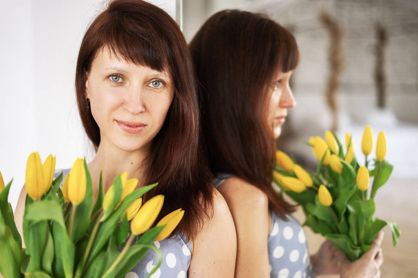 Uma jovem em um vestido azul com um grande buquê de tulipas amarelas no espelho do paciente
. - Foto, Imagem