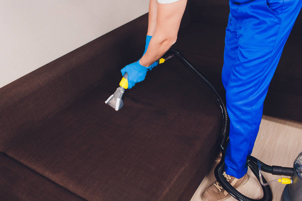Sofa chemical cleaning with professionally extraction method. Upholstered furniture. Early spring cleaning or regular clean up. Dry cleaners in light blue protective glove employee removing dirt from - Photo, image