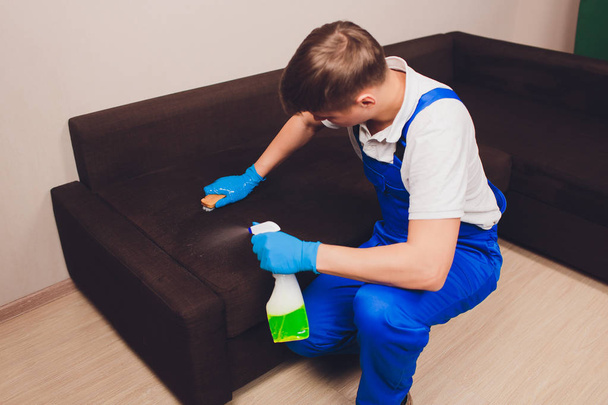 Imagen recortada. Concepto de limpieza. Mano masculina en guantes protectores limpieza sofá sofá en la habitación
. - Foto, imagen