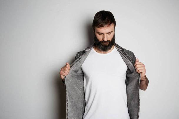 Positive brutal bearded male model poses in black jeans shirt and blank white t-shirt premium summer cotton, on white background. - Fotoğraf, Görsel