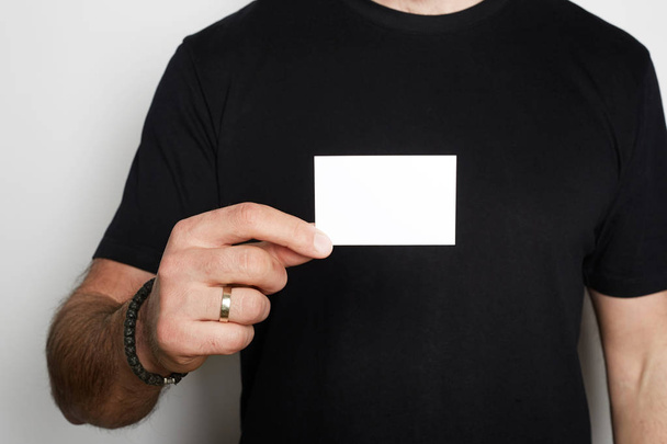 Male model poses in casual blank black t-shirt premium summer cotton and holding hand empty white business card on white background. Mockup copy paste space - Fotoğraf, Görsel