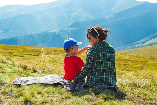 jovem mãe com criança sentada em cobertor no pico da montanha. bela paisagem vista sobre fundo
 - Foto, Imagem