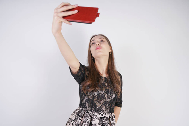 carino caucasico amichevole ragazza si trova con un telefono cellulare in mano e prende un felice selfie emotivo su uno sfondo bianco in studio da solo
 - Foto, immagini