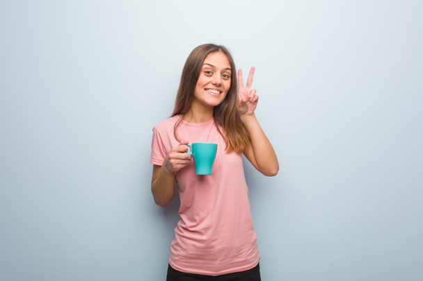 Young pretty caucasian woman fun and happy doing a gesture of victory. She is holding a mug. - Fotó, kép