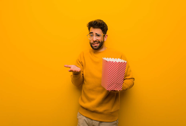 Молодий чоловік тримає попкорн збентежений і сумнівний
 - Фото, зображення