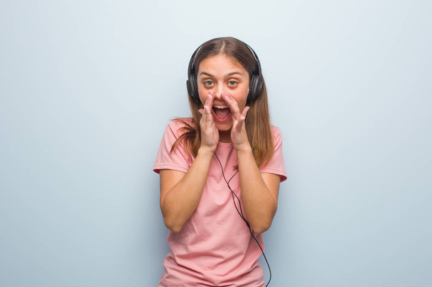 Jonge blanke vrouw schreeuwt iets vrolijks naar voren. Ze luistert naar muziek met een koptelefoon.. - Foto, afbeelding