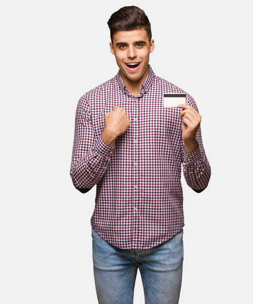 Молодой человек с кредитной картой удивлен, чувствует себя успешным и процветающим
 - Фото, изображение