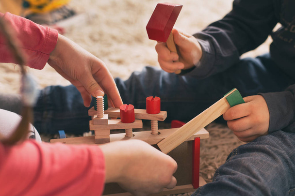 Діти грають з дерев'яними іграшками на підлозі
 - Фото, зображення