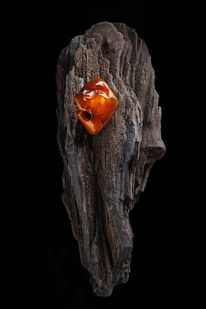 Natural amber. A piece of yellow and red semi transparent natural amber on piece of stoned wood. - Foto, imagen