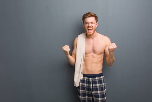 Young redhead man holding a towel surprised and shocked. He is holding a white towel. - Photo, Image