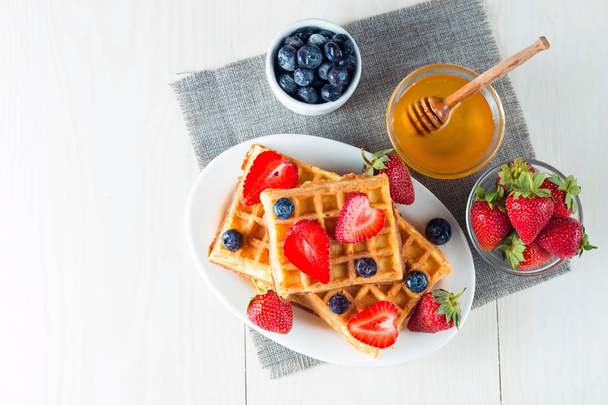 Photo of fresh homemade food made of berry Belgian waffles with honey, chocolate, strawberry, blueberry, maple syrup and cream. Healthy dessert breakfast concept with juice.  - Foto, immagini