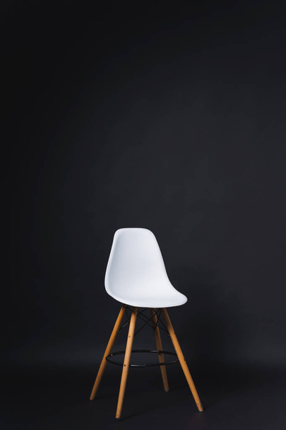 Cadeira branca em um fundo preto. Papel de fundo do estúdio. Design bar banquinho com costas de plástico e pernas de madeira
. - Foto, Imagem