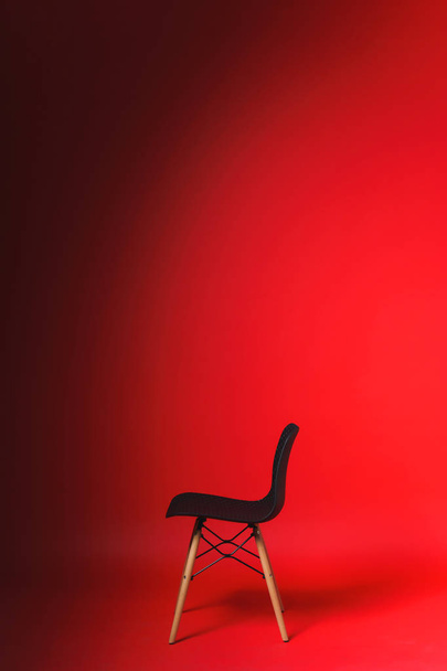 Musta tuoli punaisella taustalla. Studiopaperin tausta. Suunnittelija tuoli muovinen takaisin ja puiset jalat
. - Valokuva, kuva