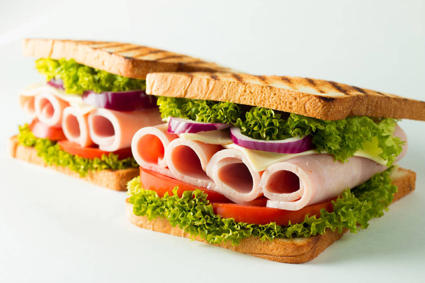 Close-up photo of a club sandwich. Sandwich with meat, prosciutto, salami, salad, vegetables, lettuce, tomato, onion and mustard on a fresh sliced rye bread on wooden background. Olives background. - Photo, Image