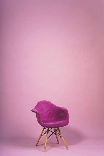 Chair on a light pink background. Studio paper background with props. Purple designer armchair with a soft back and wooden legs on a purple background. - Foto, Imagem
