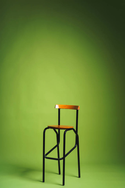 明るい緑の背景にバースツール。小道具を持つスタジオの紙の背景。金属の足が付いている木製の高い椅子. - 写真・画像