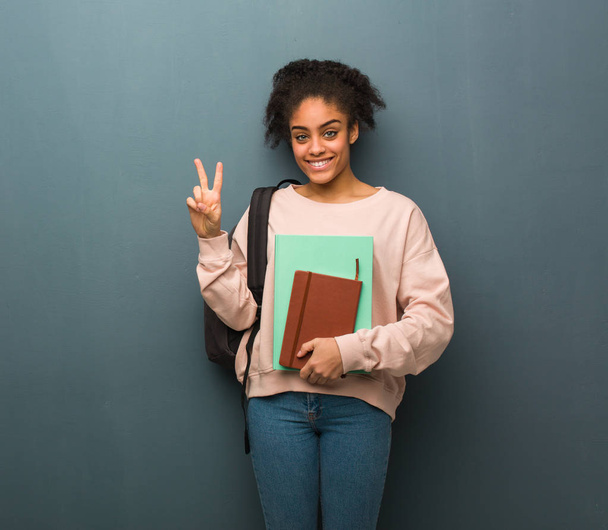 Jeune étudiante noire montrant le numéro deux. Elle tient des livres.
. - Photo, image