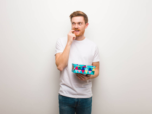 Young redhead man relaxed thinking about something looking at a copy space. Holding a gift box. - 写真・画像