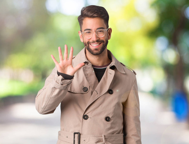 Young man wearing trench coat showing number five - Photo, Image