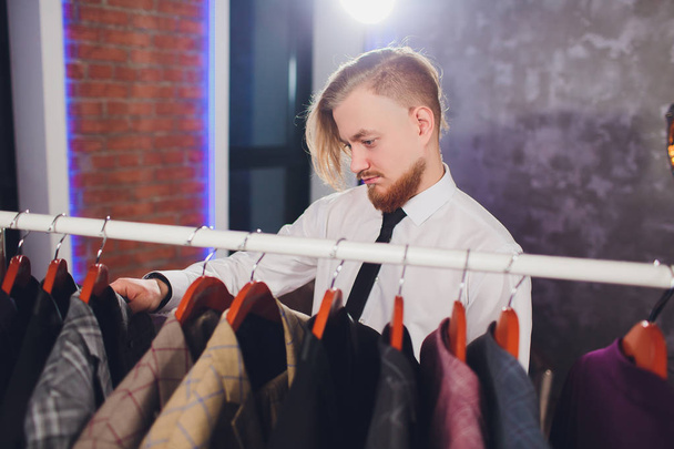 portrait of male client choosing classic jacket in the mall. - 写真・画像
