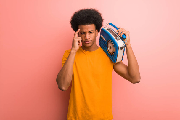 Young african american holding a vintage radio thinking about an idea - Фото, изображение