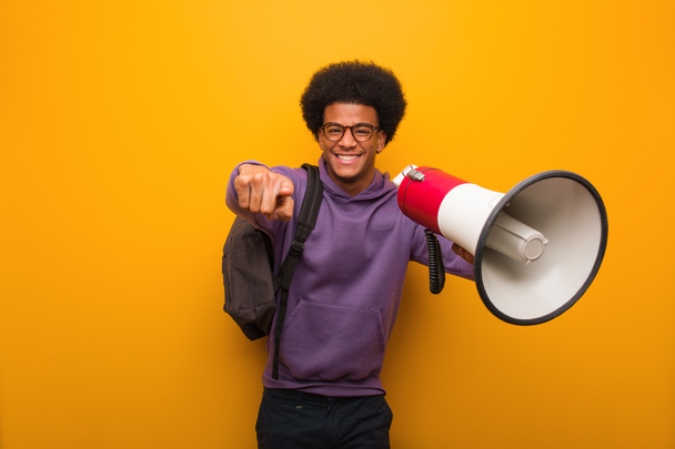 Jeune homme afro-américain tenant un mégaphone joyeux et souriant pointant vers l'avant
 - Photo, image