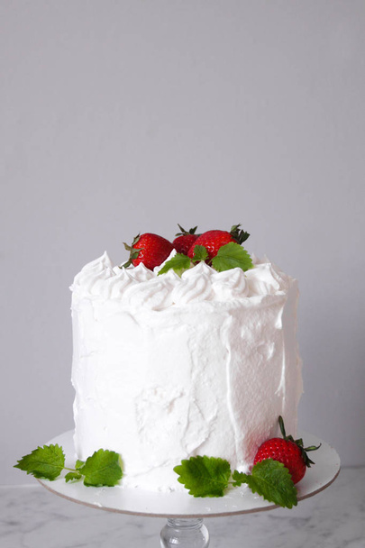 Large white delicious cake with cream and decorated with strawberries and mint on a transparent stand on a gray background   - Foto, immagini