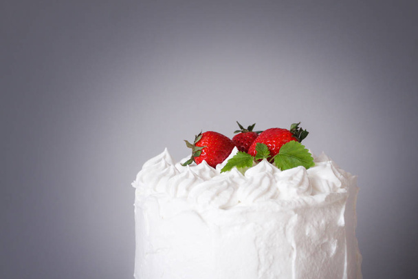 Large white delicious cake with cream and decorated with strawberries and mint on a transparent stand on a gray background   - Fotoğraf, Görsel